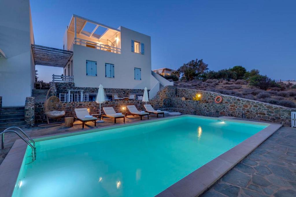 a swimming pool with chairs and a house in the background at Aqua Blu Syros 1,3 in Posidhonía