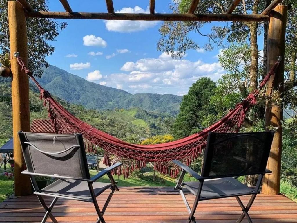 Duas cadeiras e uma rede de descanso num deque com vista em Chalé Madeira Rústica em Visconde de Mauá