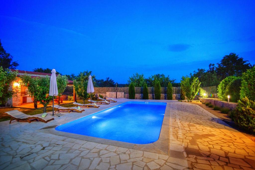 a swimming pool in a backyard at night with chairs and umbrellas at Villa Prima Natura, Imotski private pool in Imotski