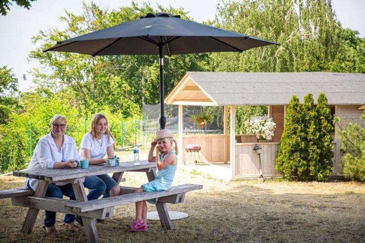 two women and a child sitting at a picnic table with an umbrella at Bungalow, Miedzyzdroje in Międzyzdroje