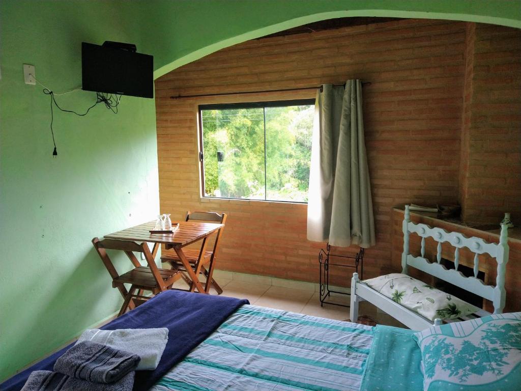 ein Schlafzimmer mit einem Bett und einem Tisch und einem Fenster in der Unterkunft Sitio Pousada Morada do Sol in Cunha