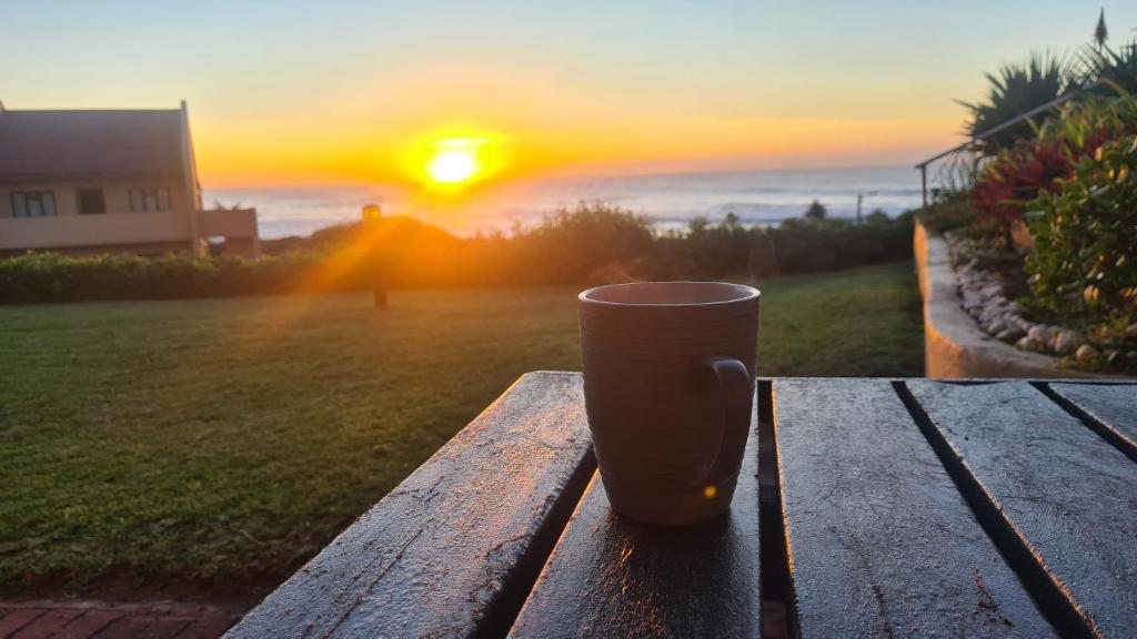 una taza de café sentada en una mesa de madera con la puesta de sol en Eden Dunes - Shelly Beach, en Margate