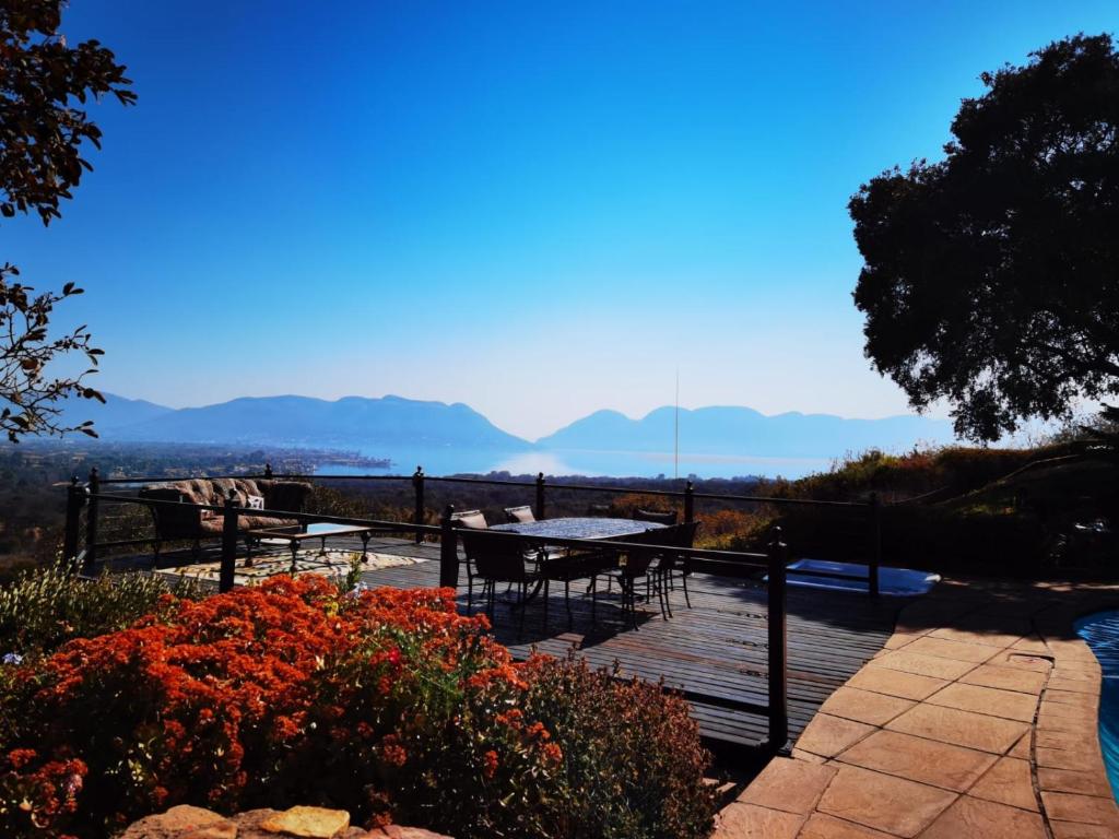 Una terraza de madera con mesas, sillas y flores. en La Montagne Guest Lodge, en Hartbeespoort
