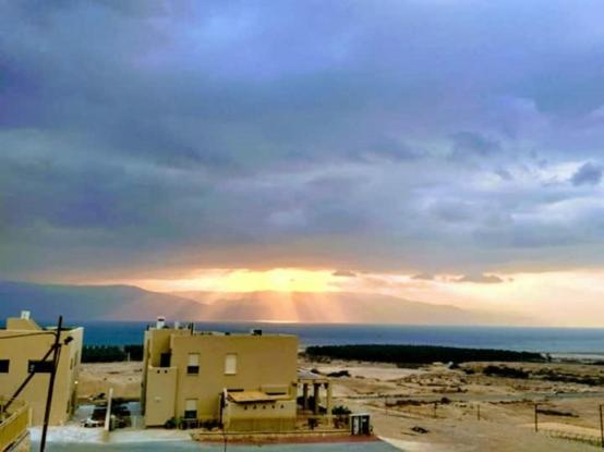 a rainbow in the sky over the ocean with a building at Dead sea families unit in Ovnat