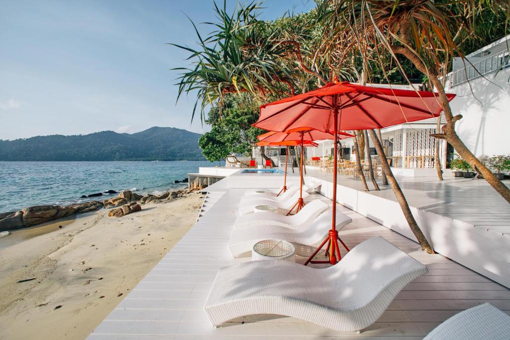 uma fila de cadeiras brancas e um guarda-sol na praia em Casa De Lipe em Ko Lipe