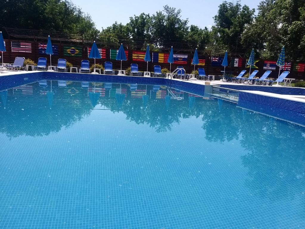 uma grande piscina com cadeiras e guarda-sóis azuis em Къща за гости "Там край реката " em Slivek