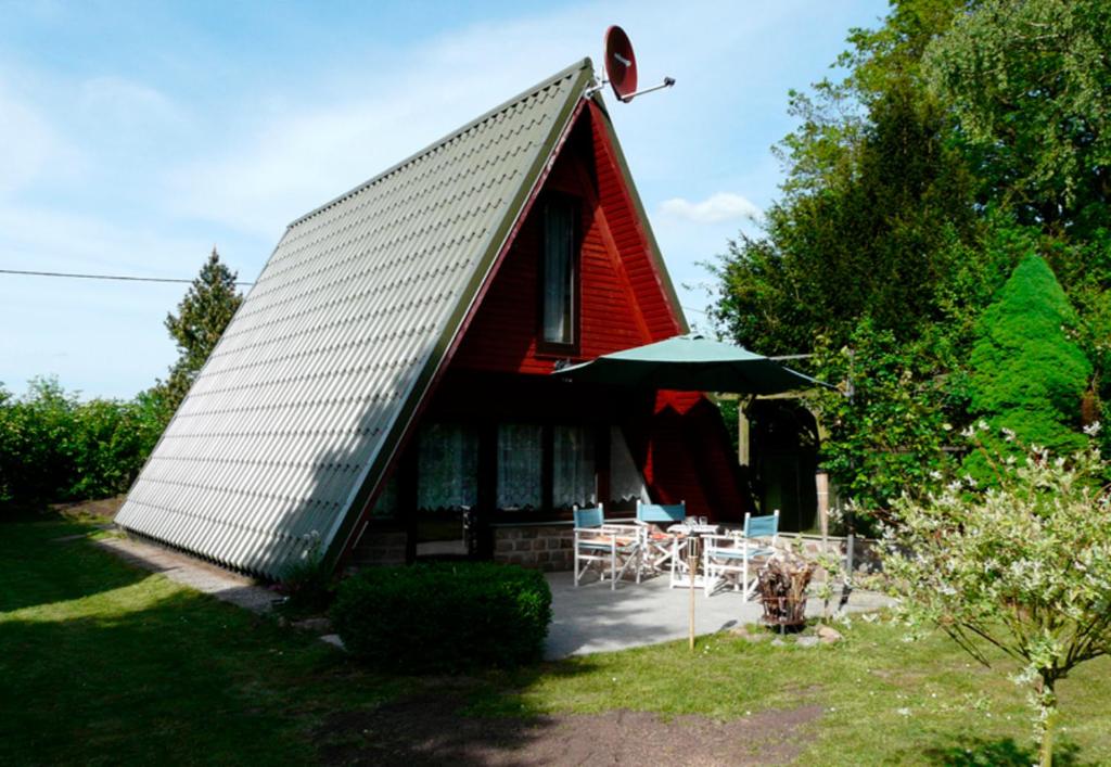 una casa con techo rojo con sillas y sombrilla en Ferienhaus am See - a55956, en Perlin