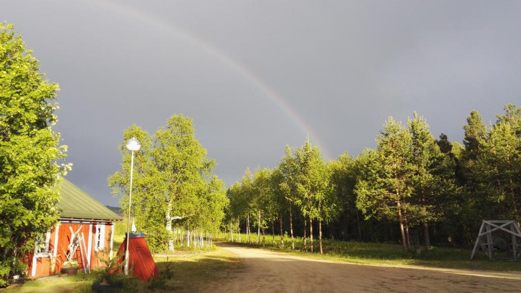 a dirt road with trees and a building and a rainbow in the sky at Lomakylä Lapponia in Inari