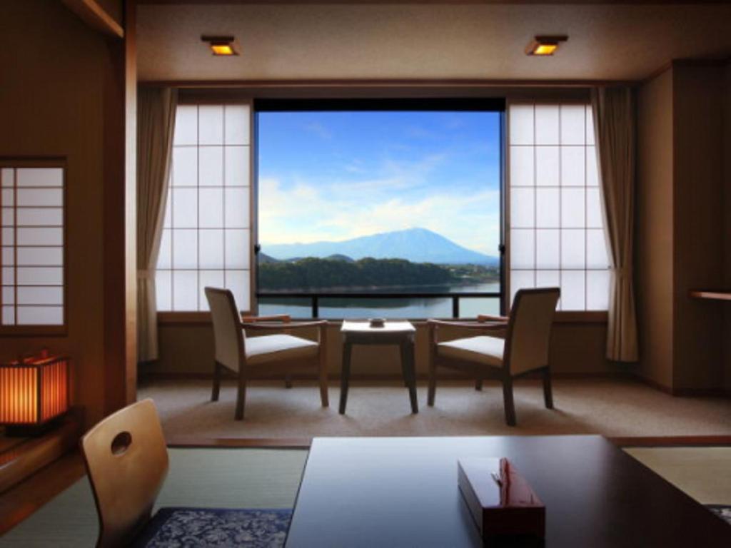 a living room with a table and chairs and a large window at Hotel Shion in Morioka