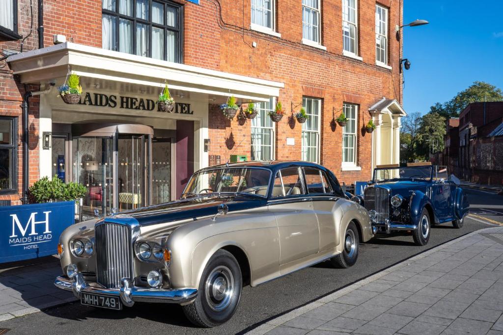 two old cars parked in front of a building at The Maids Head Hotel in Norwich