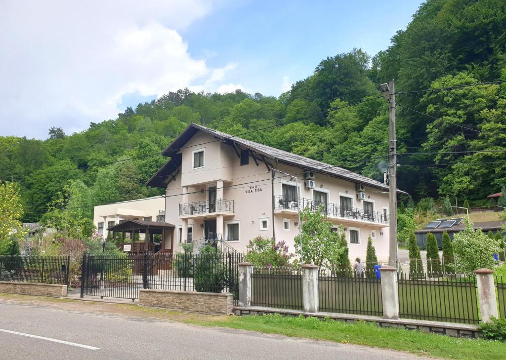 a white house with a fence next to a road at Vila Tisa in Tismana