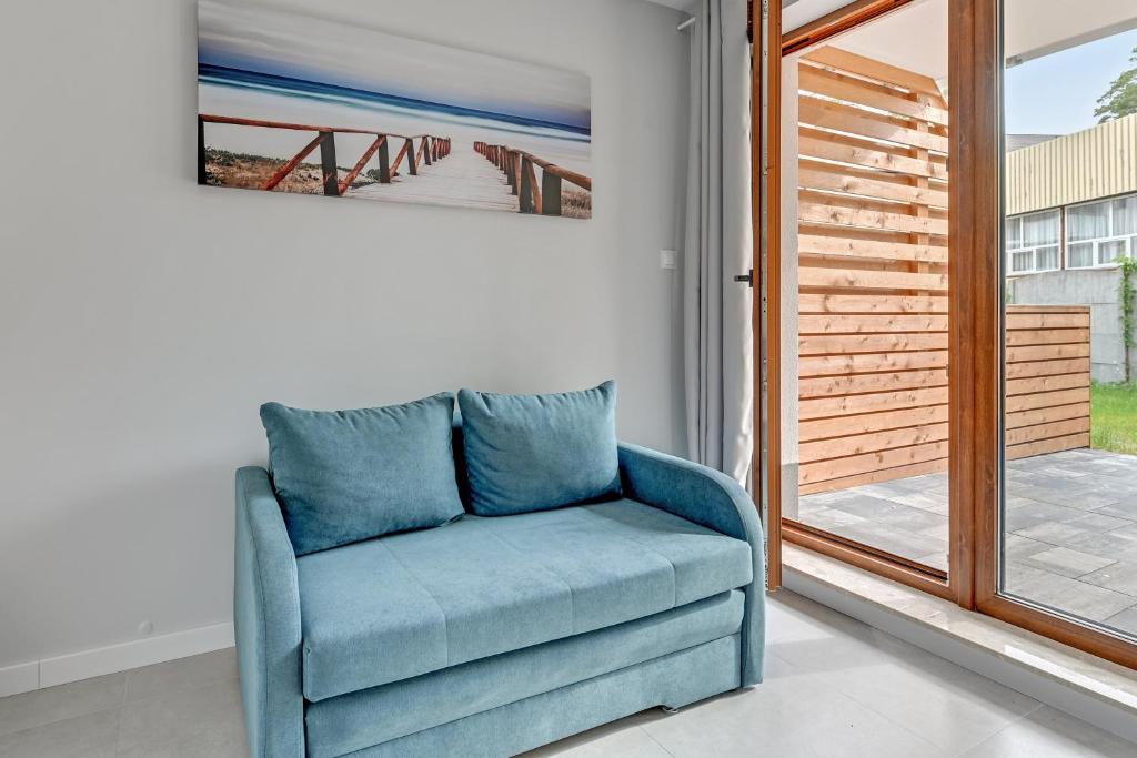 Small blue loveseat beside patio doors, seaside artwork above, serene natural light.