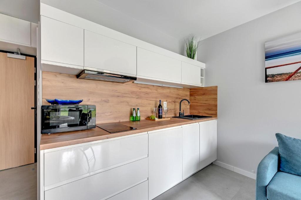 Sleek white kitchenette with wooden countertop, microwave, sink and bottled drinks.