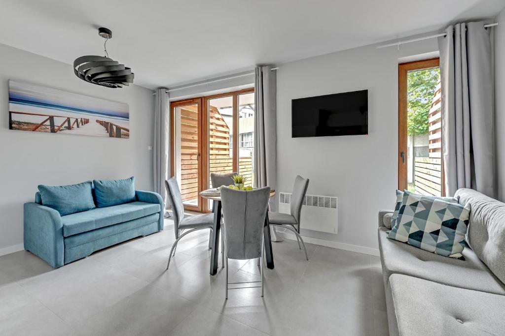 Sunlit open-plan living area with dining table, grey chairs, blue sofa and wall art.