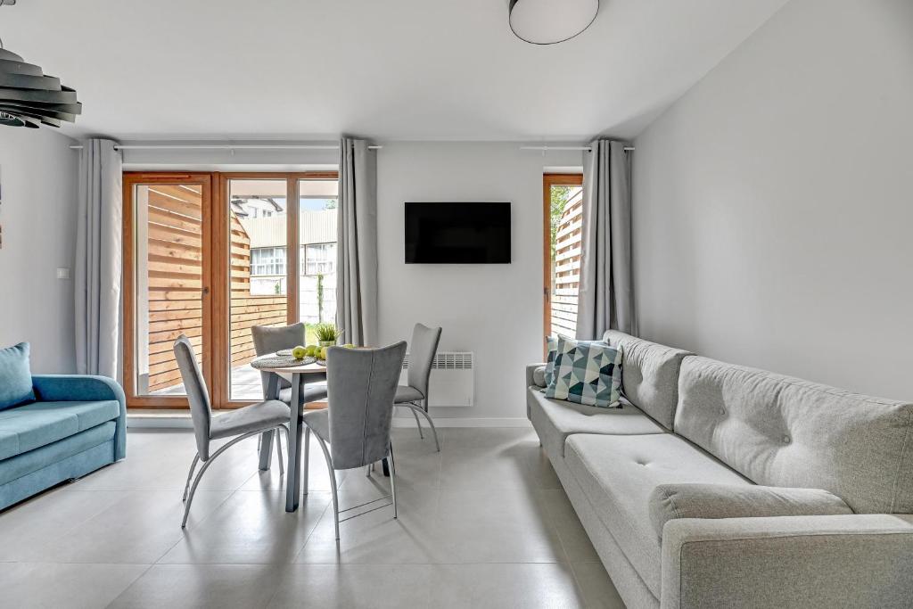Bright modern living room with grey sofa, round dining table, blue loveseat, wall-mounted TV.