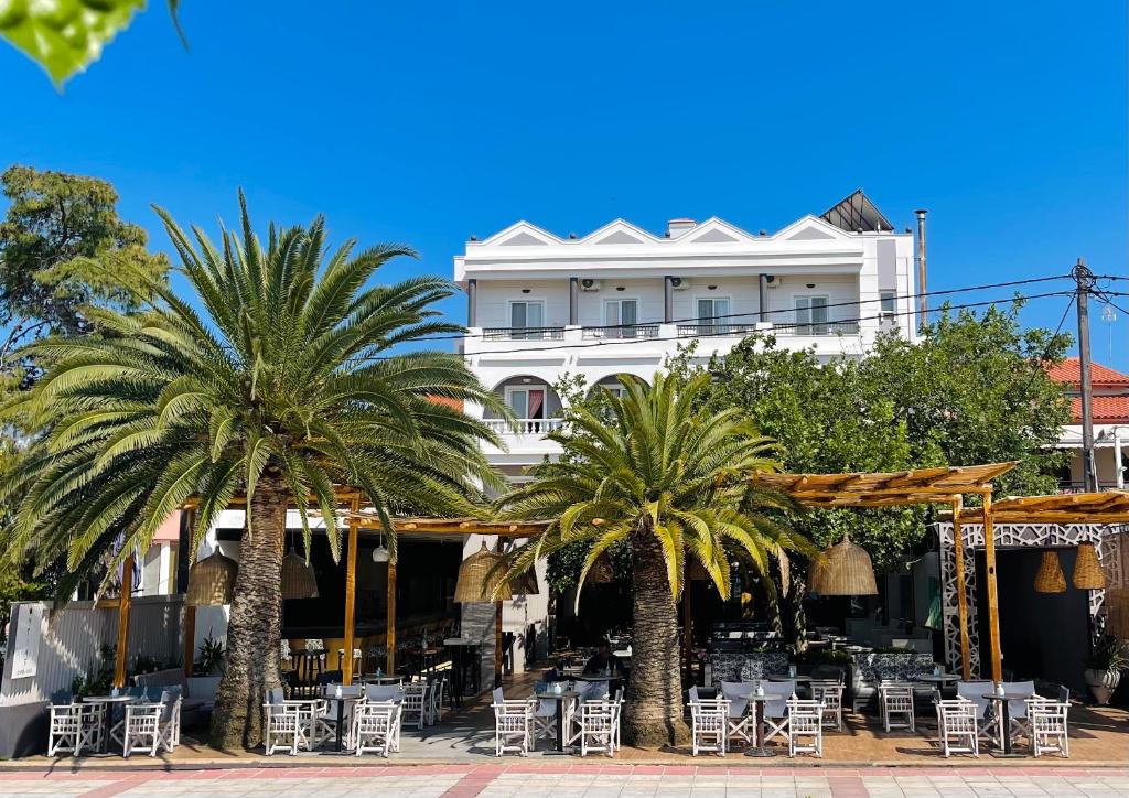 a white building with palm trees and tables and chairs at Galini Hotel in Pefki