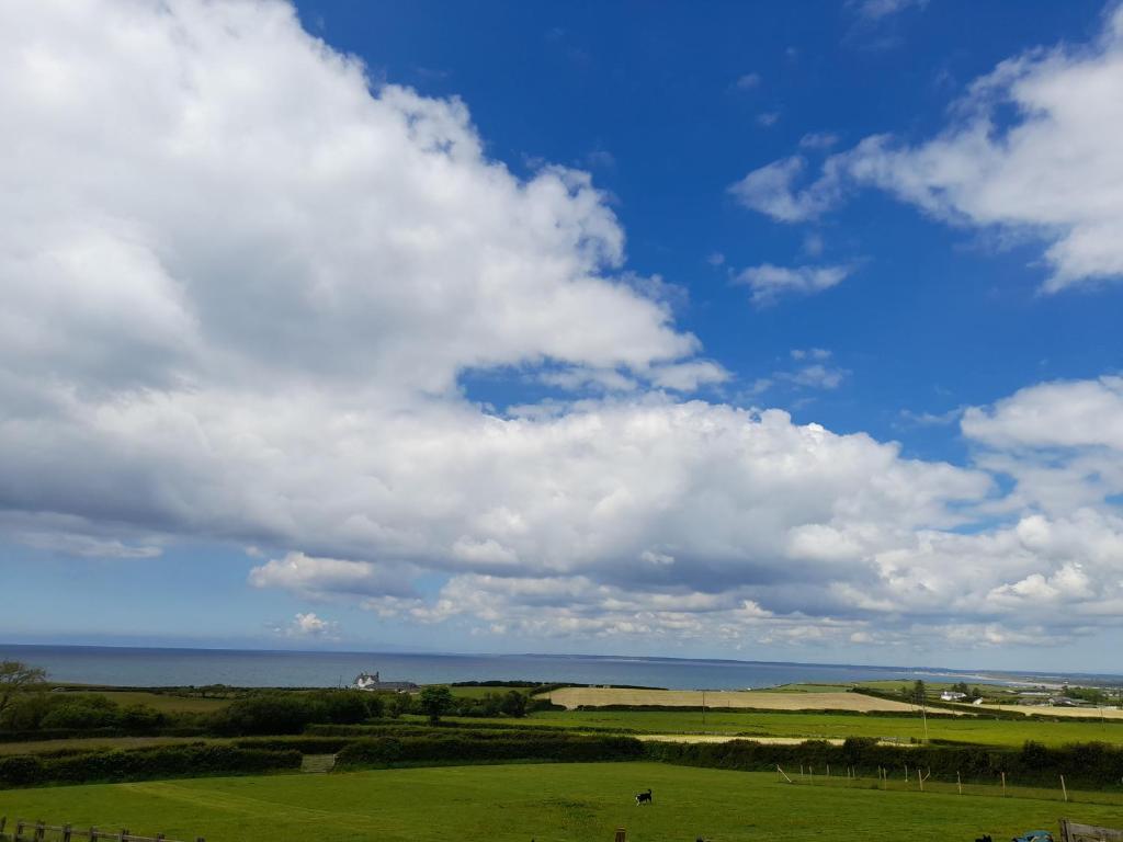 un campo con un cielo nublado y el océano en Gilfach en Clynnog-fawr