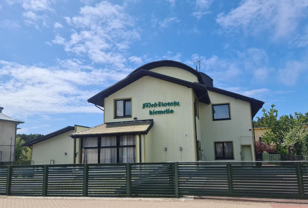 a white building with a black roof and a fence at Medziotoju kiemelis in Palanga