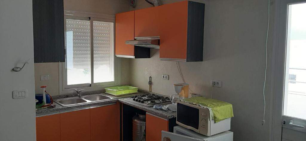 a kitchen with orange cabinets and a sink and a microwave at bel appart terasse vue panoramique avec piscine in Ariana