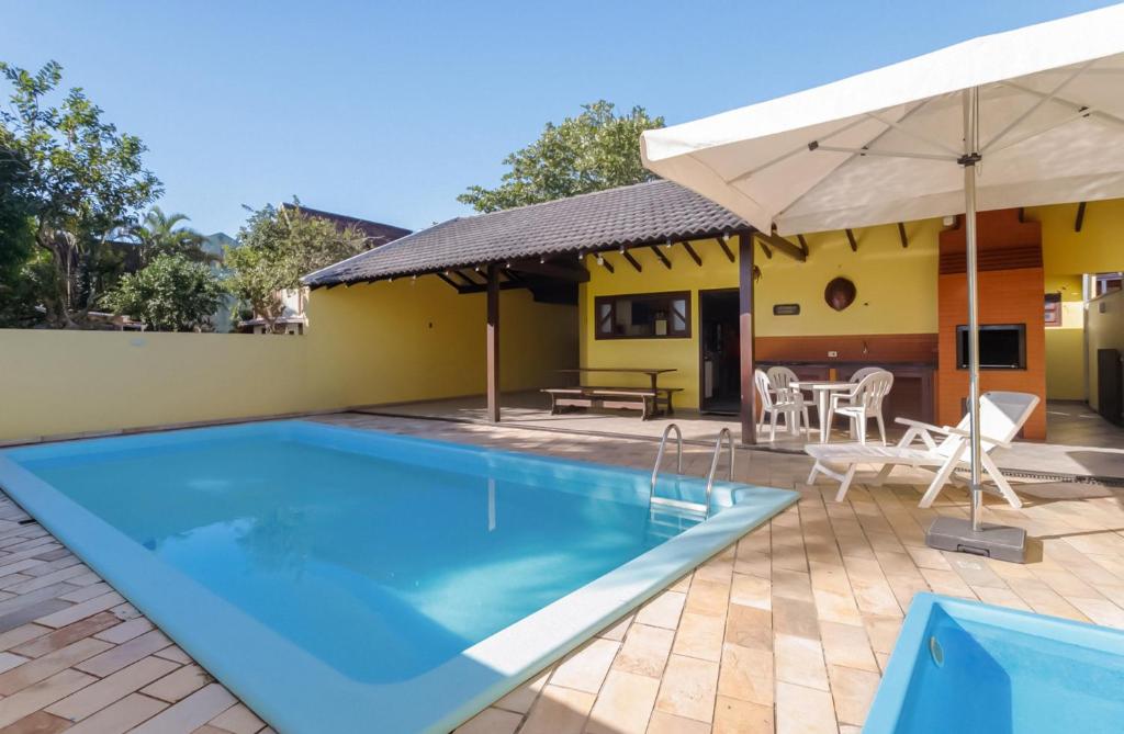 a swimming pool with an umbrella and a house at Casa Guaratuba-Barra do Saí - "Recanto de Milady" - 80 m da Praia in Guaratuba