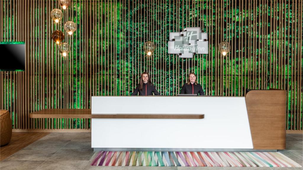 two people standing behind a reception desk in front of a green wall at Holiday Inn Munich - Leuchtenbergring, an IHG Hotel in Munich
