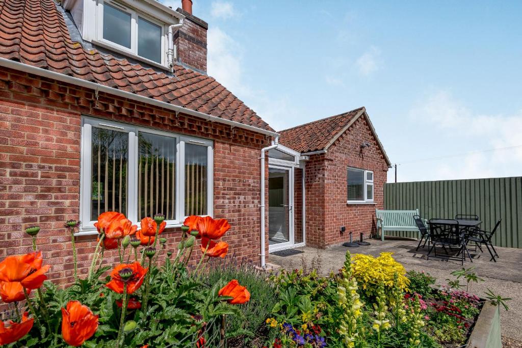 a brick house with red flowers in the yard at Woodland View in West Barkwith