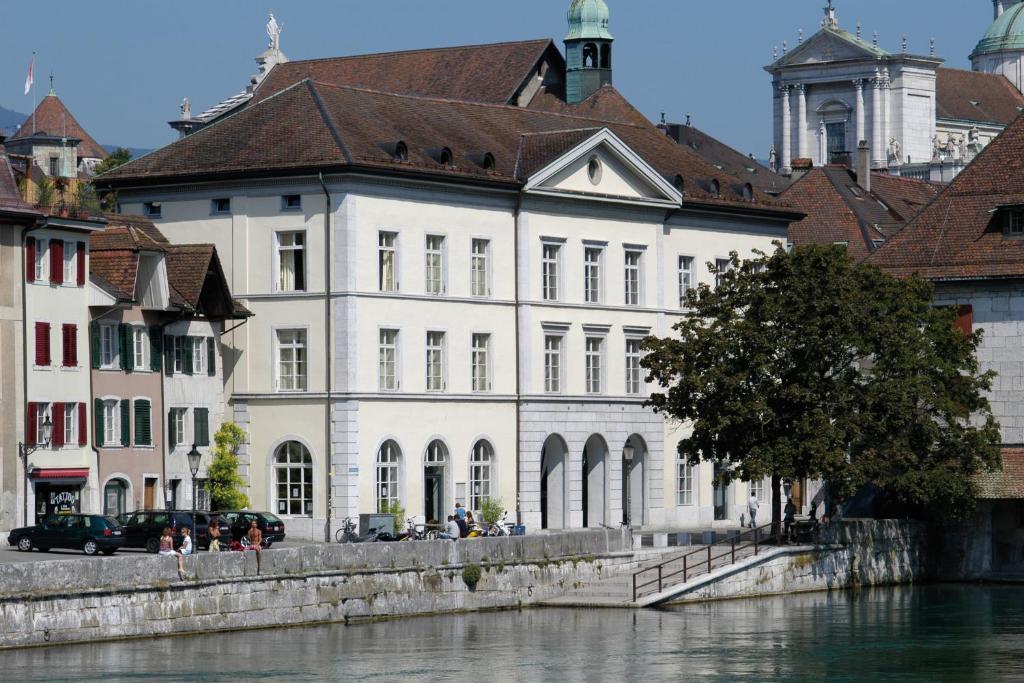 a white building with a brown roof next to a river at Solothurn Youth Hostel in Solothurn