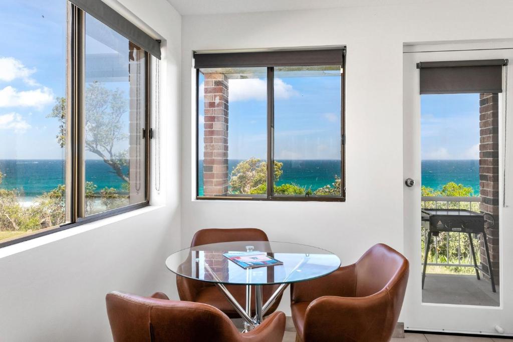 a room with a table and chairs and windows at South Pacific Studio in Ulladulla