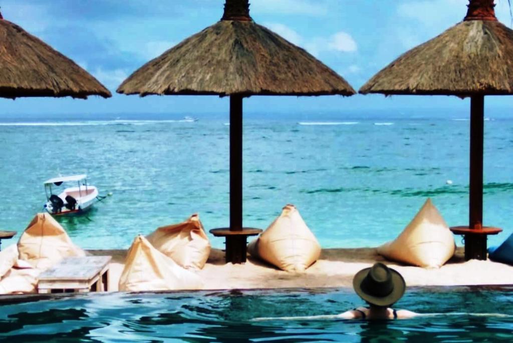 a resort swimming pool with umbrellas and the ocean at Pemedal Beach Resort in Nusa Lembongan