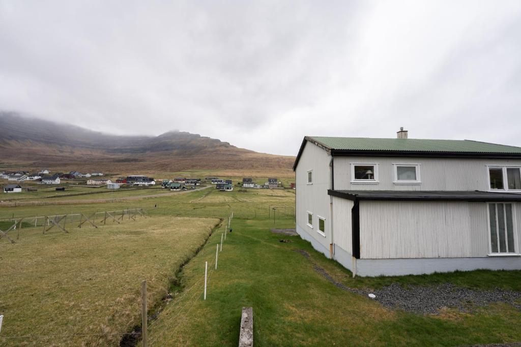 una casa bianca in un campo con montagne sullo sfondo di Scenic Village / Nature / Cozy House / 4 BR a Viðareiði