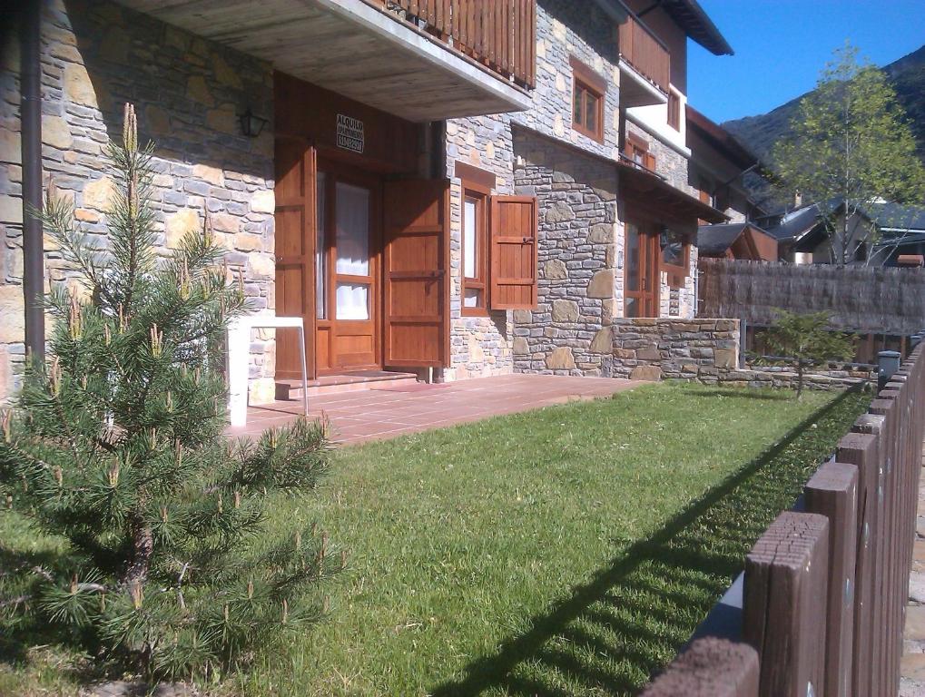 a house with a grass yard and a wooden door at APARTMENTSUITESPAIN BAQUEIRA JARDIn in Esterri d'Àneu