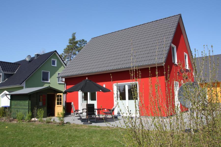 ein rotes und grünes Haus mit einem Tisch und einem Sonnenschirm in der Unterkunft K77 - 5 Sterne Ferienhaus mit Sauna, grossem Garten direkt am See in Roebel an der Mueritz in Marienfelde