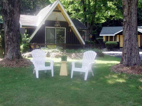 three white chairs sitting in the grass in front of a house at Amber Lantern Two-Bedroom Cottage in Lake George