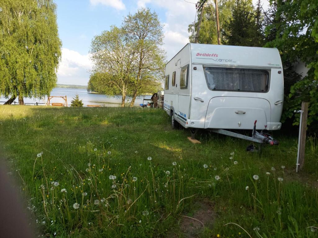 a white caravan parked in the grass next to a lake at Wilimy Przyczepa Campingowa nad jeziorem Dadaj in Wilimy