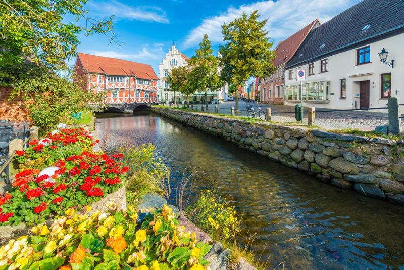 a river in a town with flowers and buildings at Ferienwohnungen im Gewölbe in Wismar
