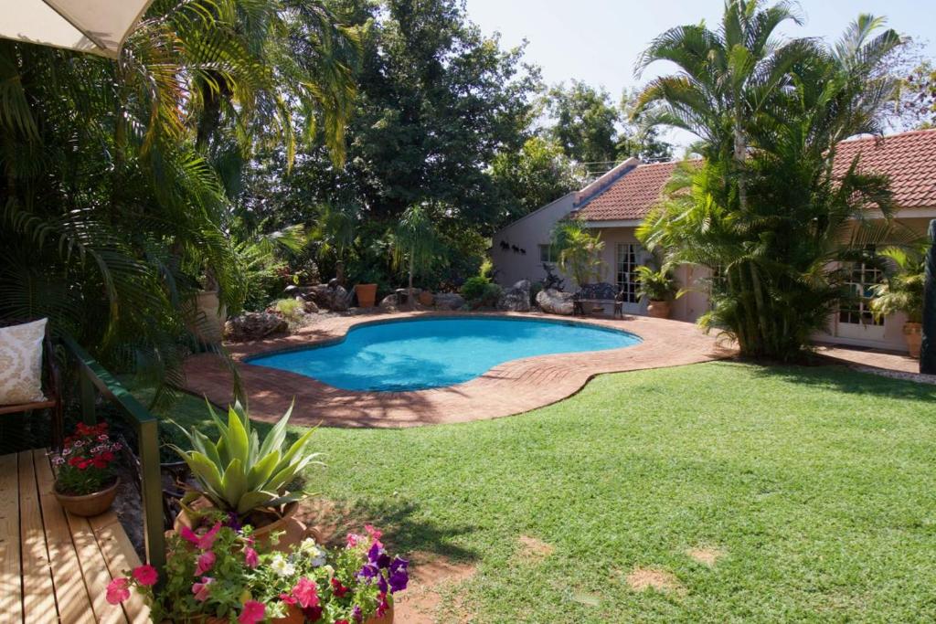 a backyard with a swimming pool and a lawn with flowers at Wonderfully spacious two bedroom cottage in a quiet secluded area of town, on the edge of the bush - 1998 in Victoria Falls