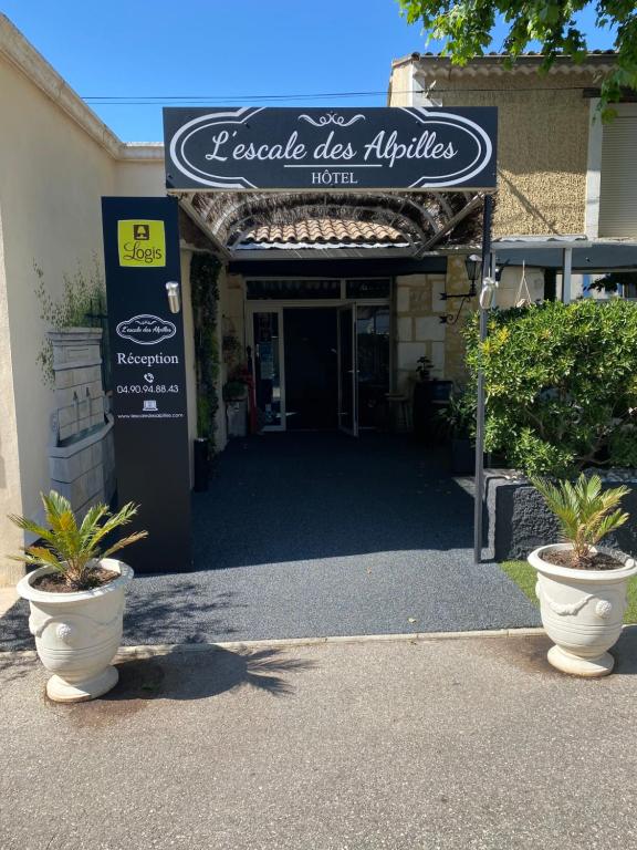 un panneau pour un magasin avec deux plantes en pot devant dans l'établissement L'Escale des Alpilles, à Rognonas