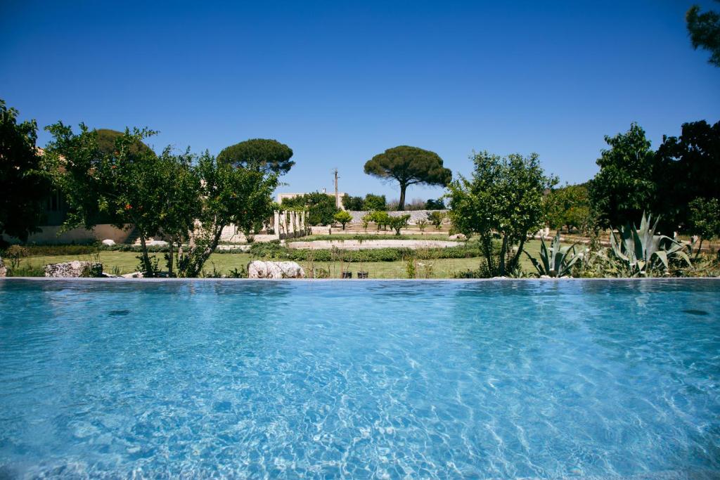 Una piscina de agua azul con árboles al fondo. en MASSERIA LILEI, en Lizzanello