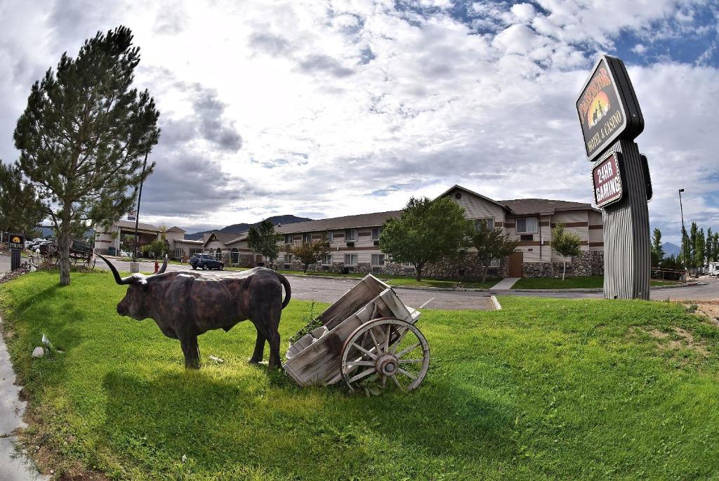 una vaca parada junto a un carro en el césped en Prospector Hotel & Casino en Ely