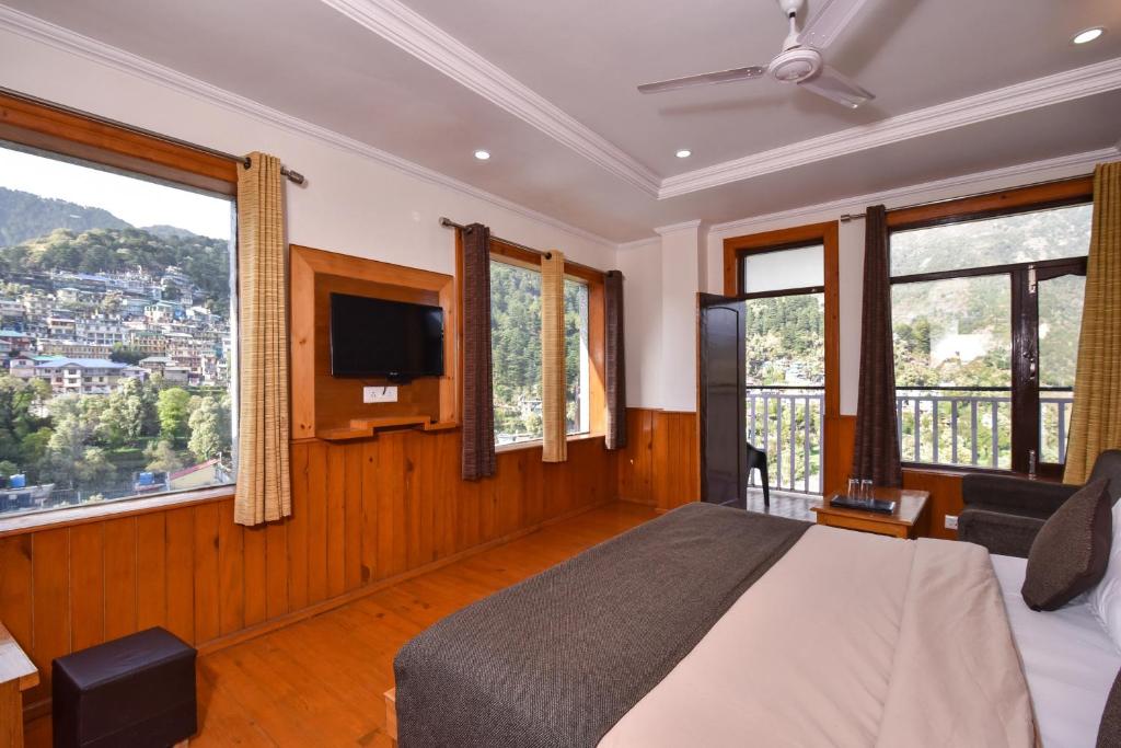 um quarto com uma cama, uma televisão e janelas em The Posh Hotel em McLeod Ganj