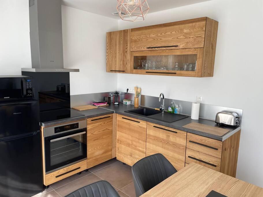 une cuisine avec des armoires en bois et un appareil noir dans l'établissement Maison Fleurs de Lys, climatisée, WiFi et Parking Privée Gratuit, Lave-Linge, Vernon Giverny, à Vernon