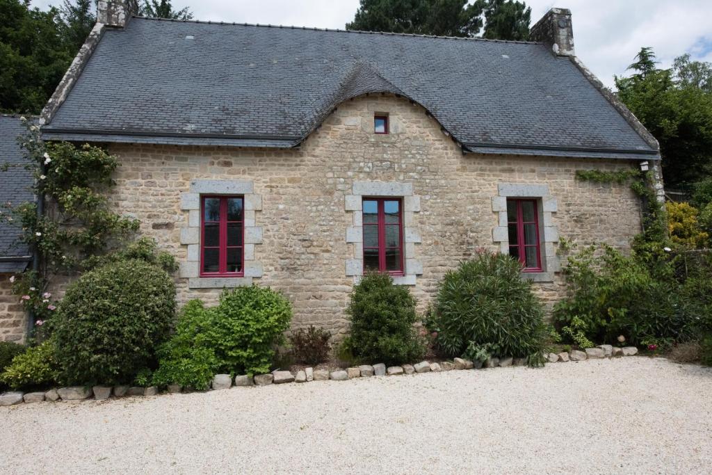 a stone house with red windows and bushes at maison bretonne in Guidel