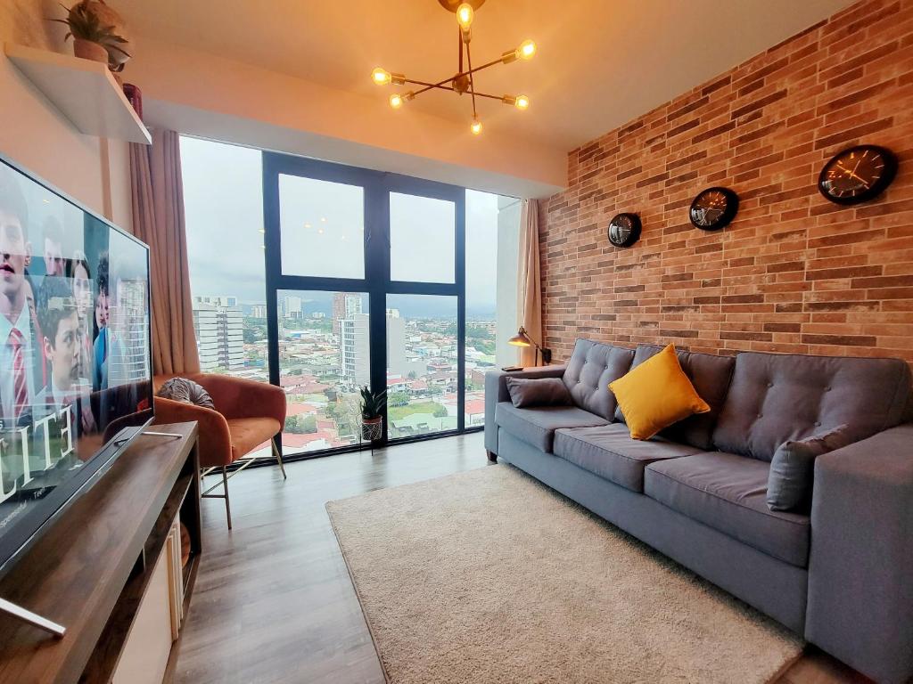 a living room with a couch and a brick wall at Cosmopolitan APT 1407, 5 Star Facilities, 15m SJO Airport, Parking, Pool, Gym in San José