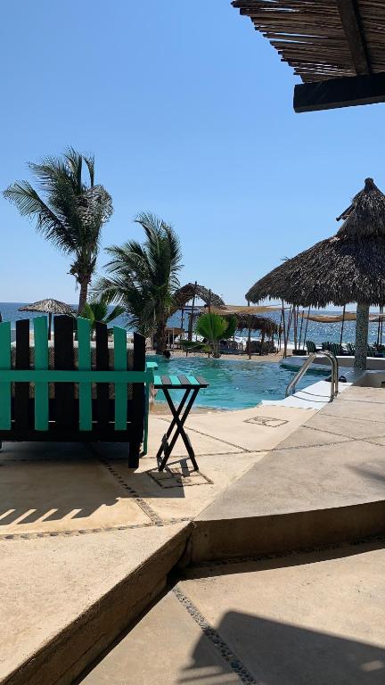 un banc vert à côté d'une piscine avec une plage dans l'établissement Condominio Agave del Mar, à Coyuca