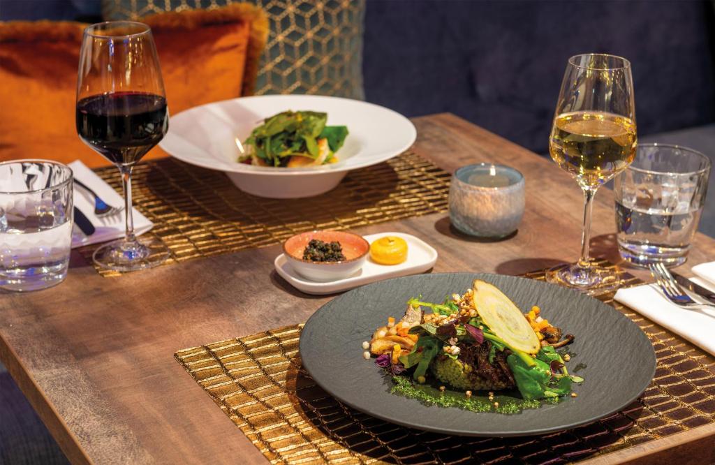 a table with a plate of food and glasses of wine at Leonardo Hotel Augsburg in Augsburg