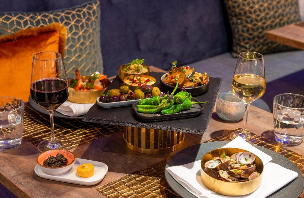 a table with plates of food and glasses of wine at Leonardo Hotel Augsburg in Augsburg