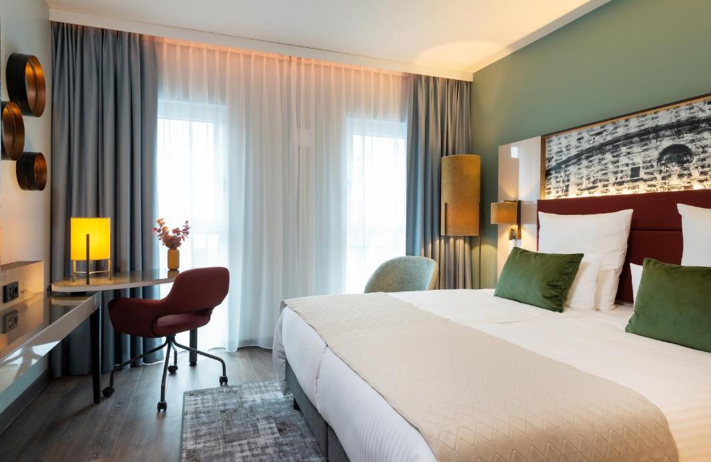 a hotel room with a large bed and a desk at Leonardo Hotel Augsburg in Augsburg