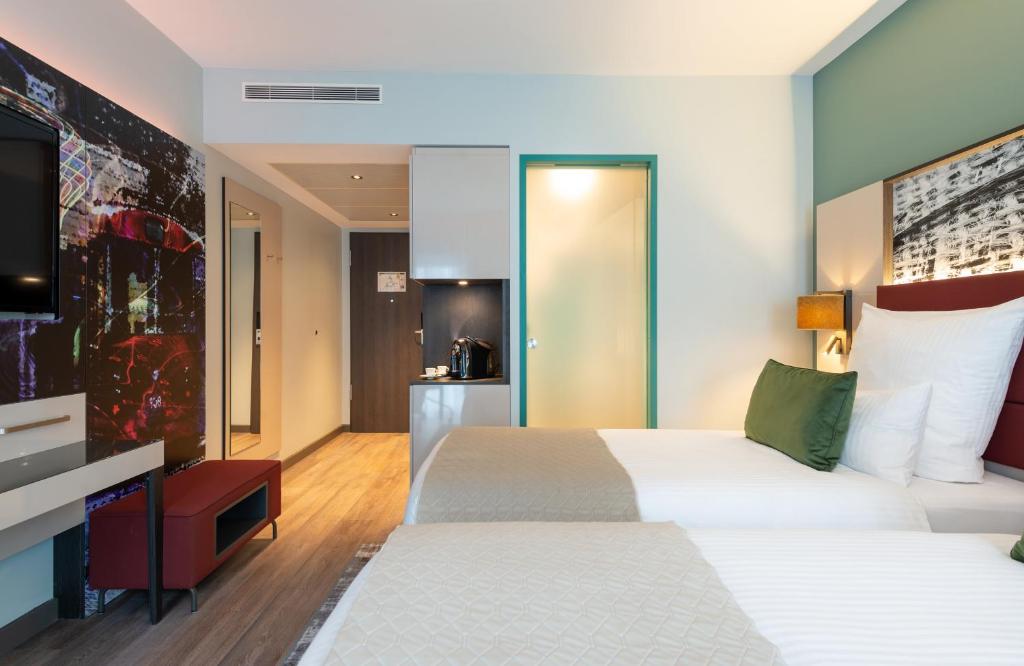 a bedroom with two beds and a flat screen tv at Leonardo Hotel Augsburg in Augsburg