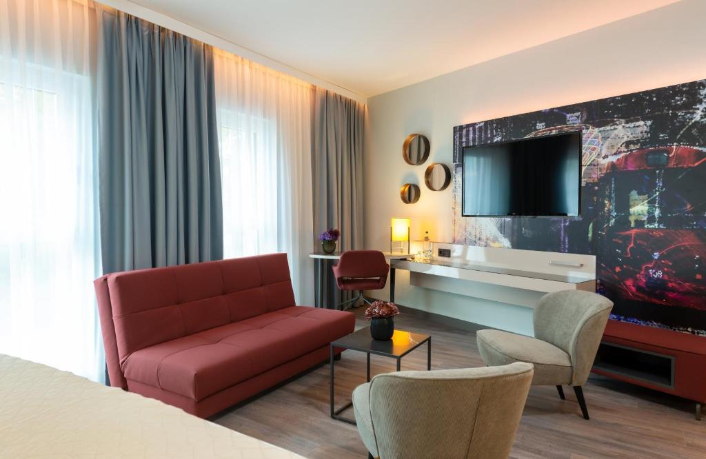 a hotel room with a red couch and a tv at Leonardo Hotel Augsburg in Augsburg