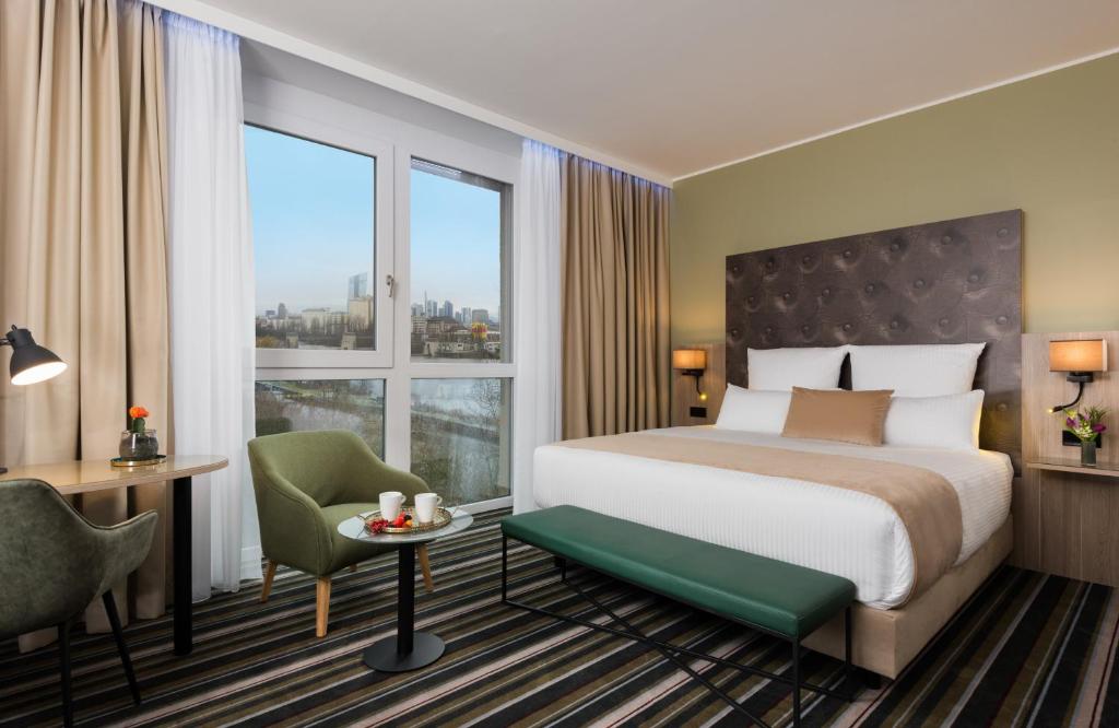 a hotel room with a bed and a desk and a window at Leonardo Hotel Offenbach Frankfurt in Offenbach